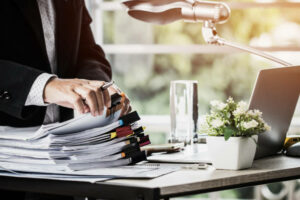 Mains d'homme d'affaires tenant un stylo pour travailler dans des piles de dossiers papier - externaliser ses services administratifs - Activ Solutions