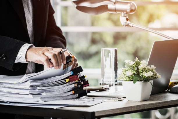 Mains d'homme d'affaires tenant un stylo pour travailler dans des piles de dossiers papier - externaliser ses services administratifs - Activ Solutions